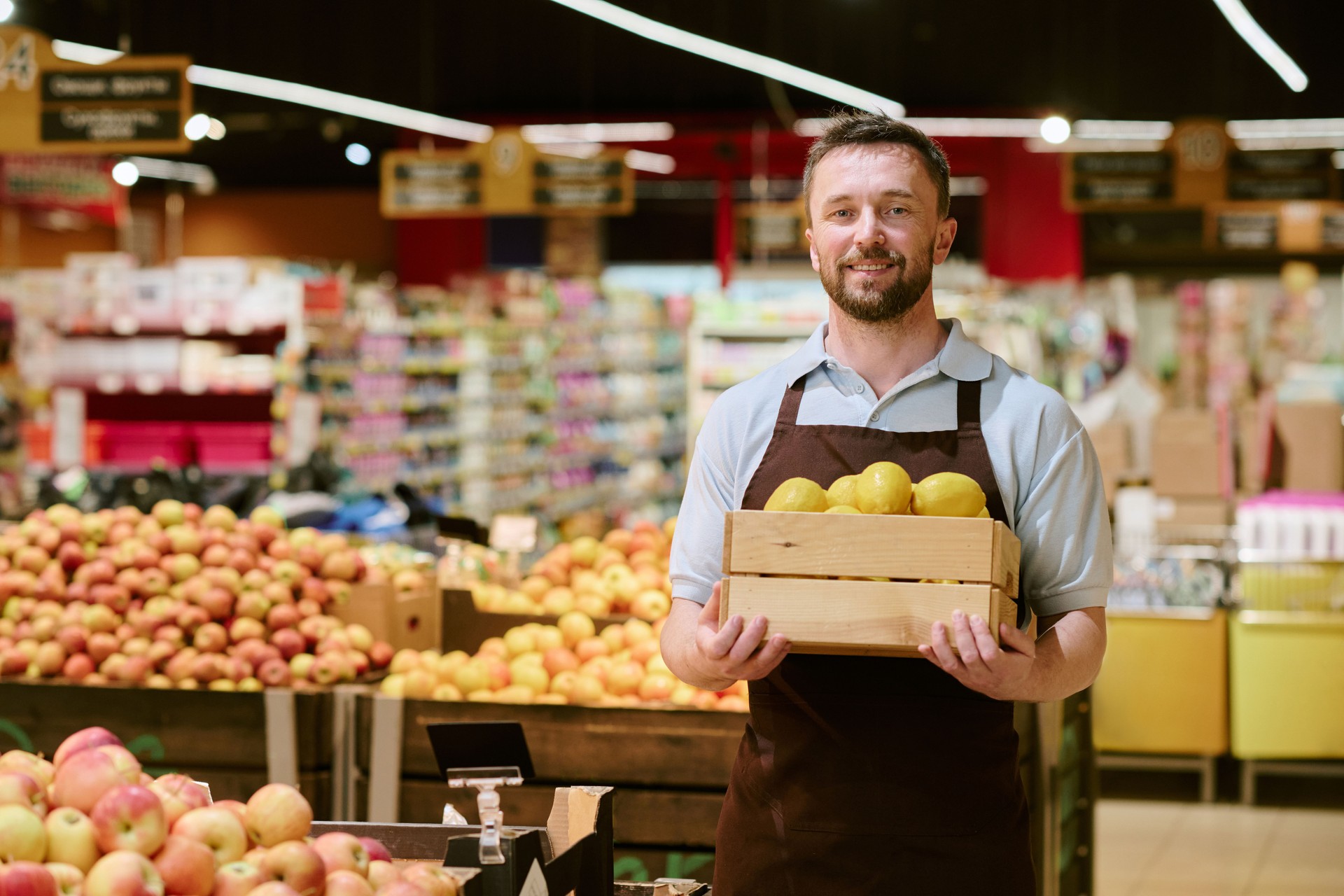 Smiling Grocer Holding Basket of Fresh Yellow Apples